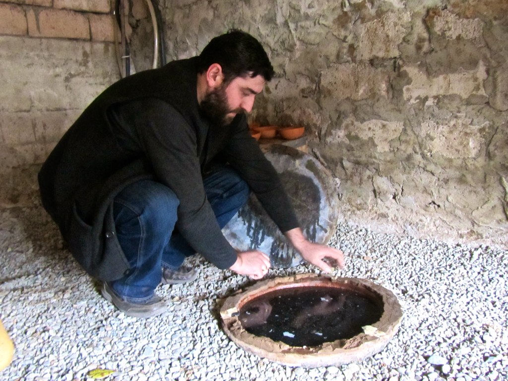 A man in Georgia scraping mud from a qvevri.