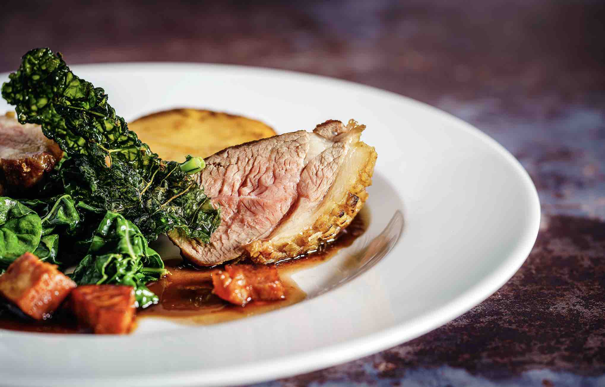 Photograph of duck breast on a plate with some vegetables